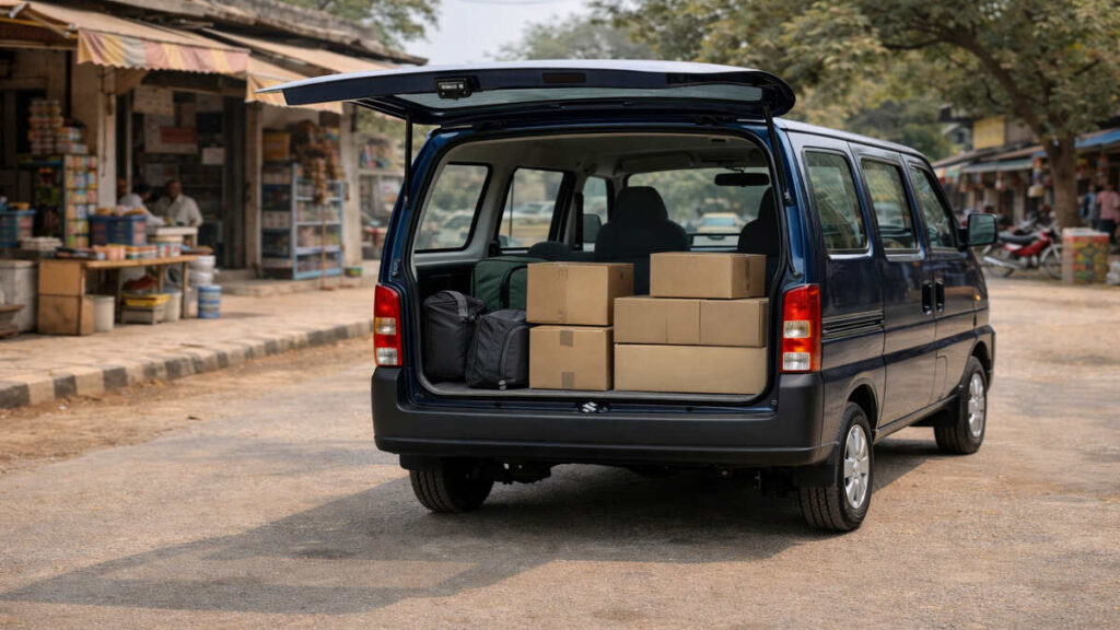 Maruti Suzuki Eeco van with rear door open showing cargo boxes near a small shop in an Indian town.